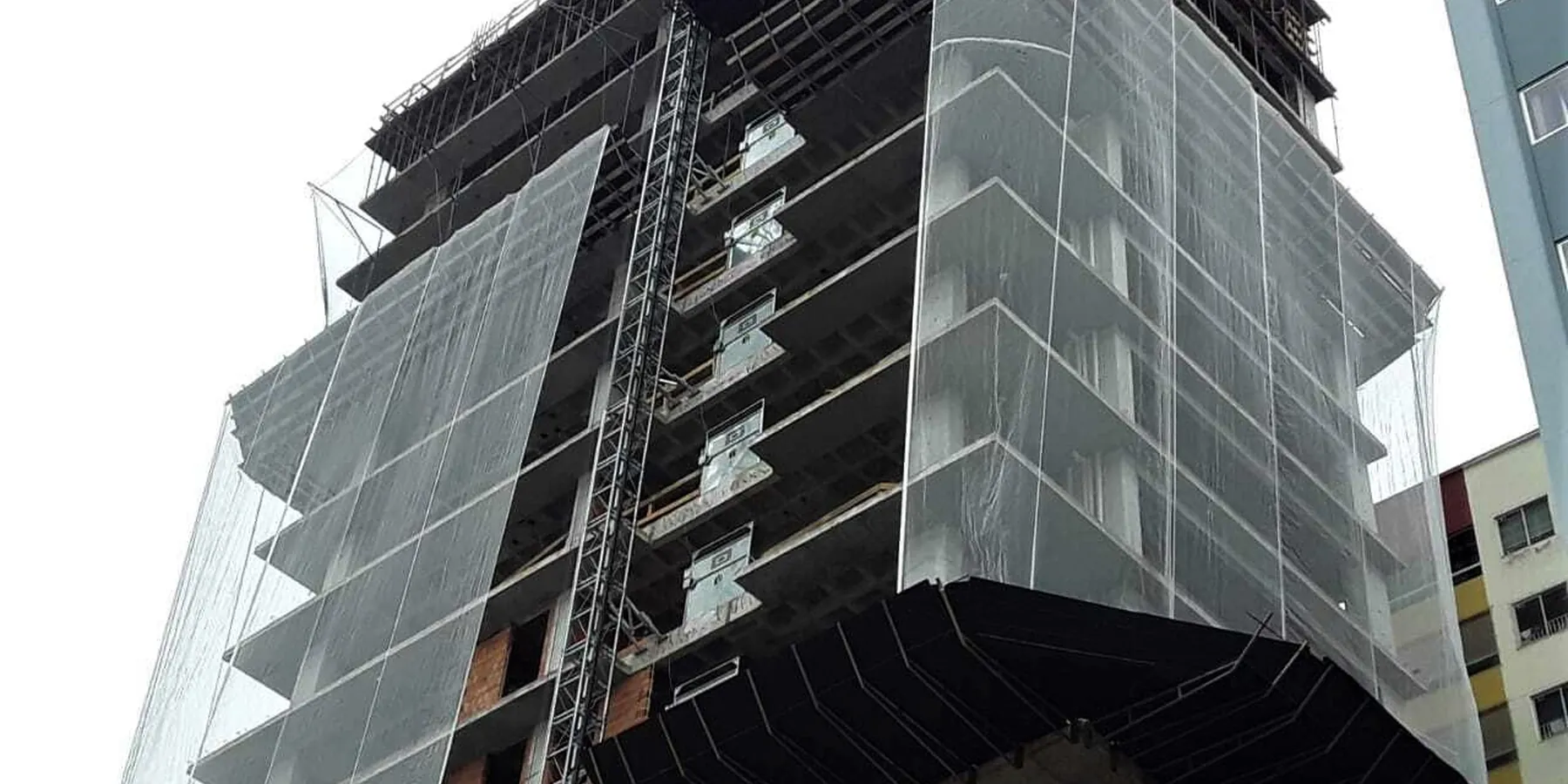 Canteiro de obras com tela fachadeira tensionada painel a painel ao redor da estrutura