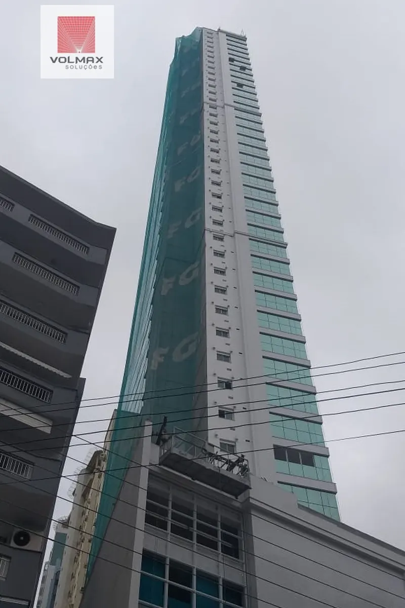 Edifício alto com tela de proteção verde e placa Volmax na base