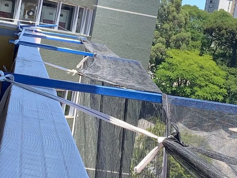 Suporte de tela fachadeira fixado na estrutura, com a rede tensionada entre pavimentos